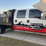 White and red commercial truck with vehicle decal on passenger side doors. Stevens Septic Service 704-201-9849
