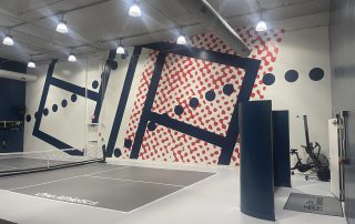 Indoor pickleball court from OneAthletics. Wall sign in gym with lack polka dot line and red puzzle paint.