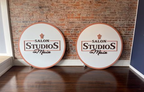 Indoor signage | Brick Wall | 2 Oval Signs with white background and dark brown letters reading, "Salon Studios on Main".